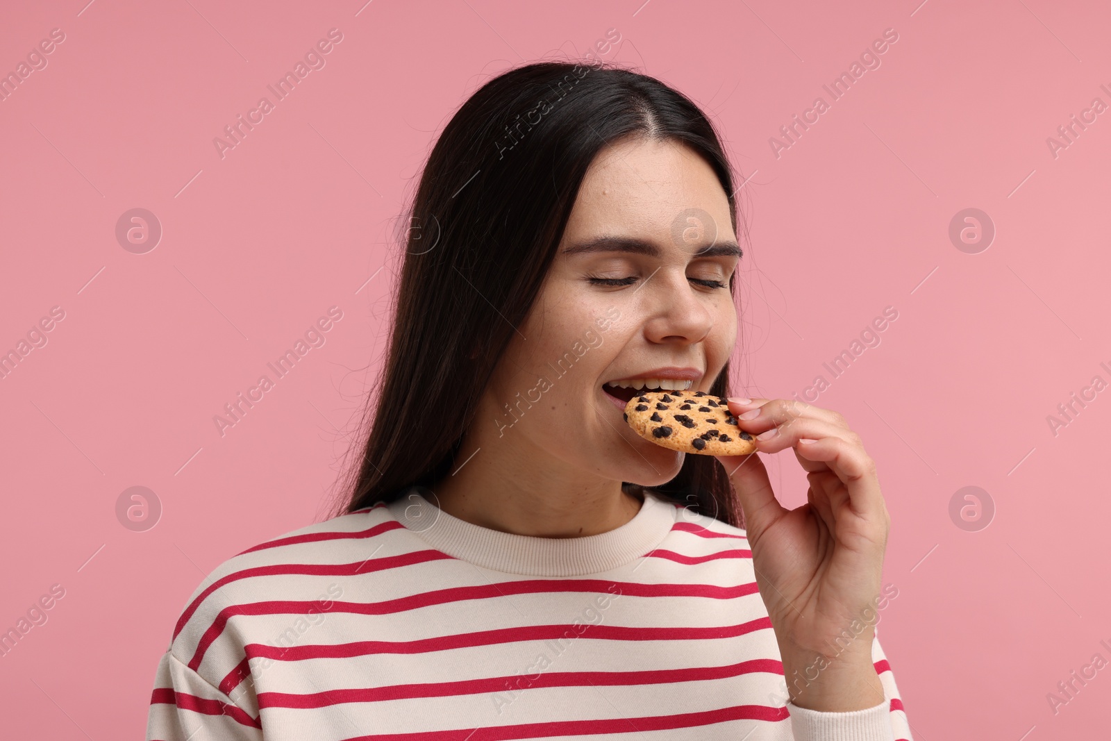 Photo of Young woman with chocolate chip cookie on pink background
