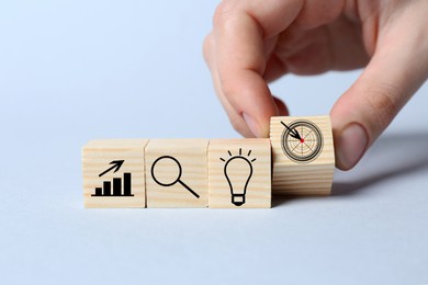 Woman putting cube with icon of target into row of others on light background, closeup