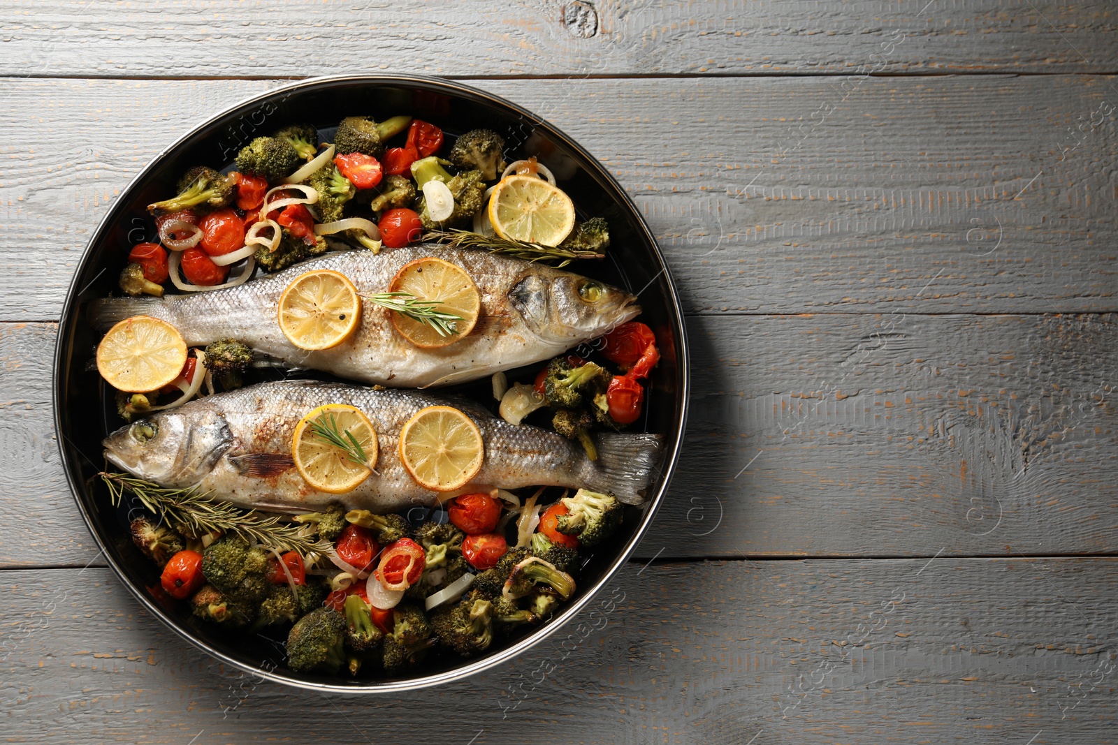 Photo of Baked fish with vegetables, rosemary and lemon on grey wooden table, top view. Space for text