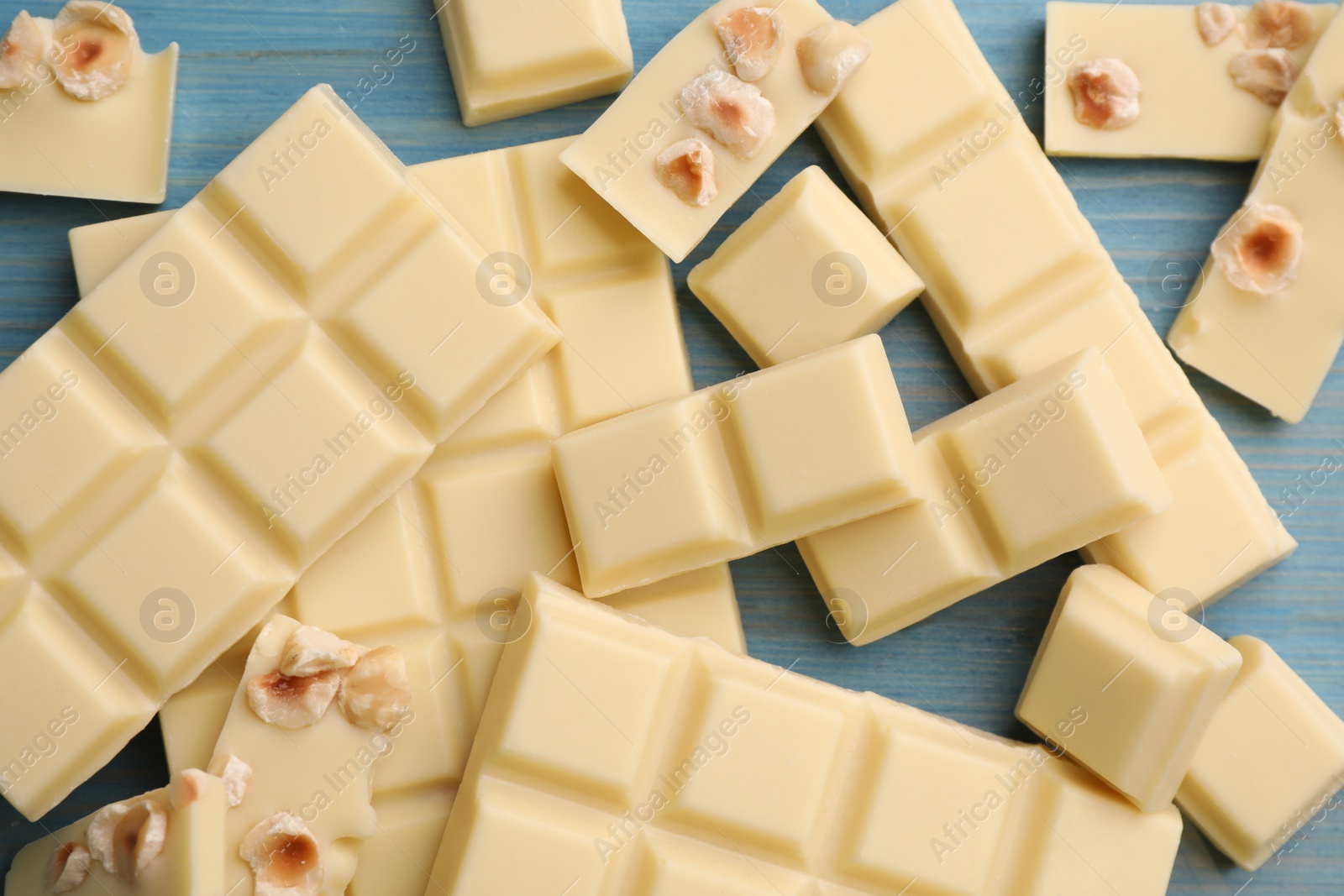 Photo of Delicious white chocolate with hazelnuts on light blue wooden table, flat lay