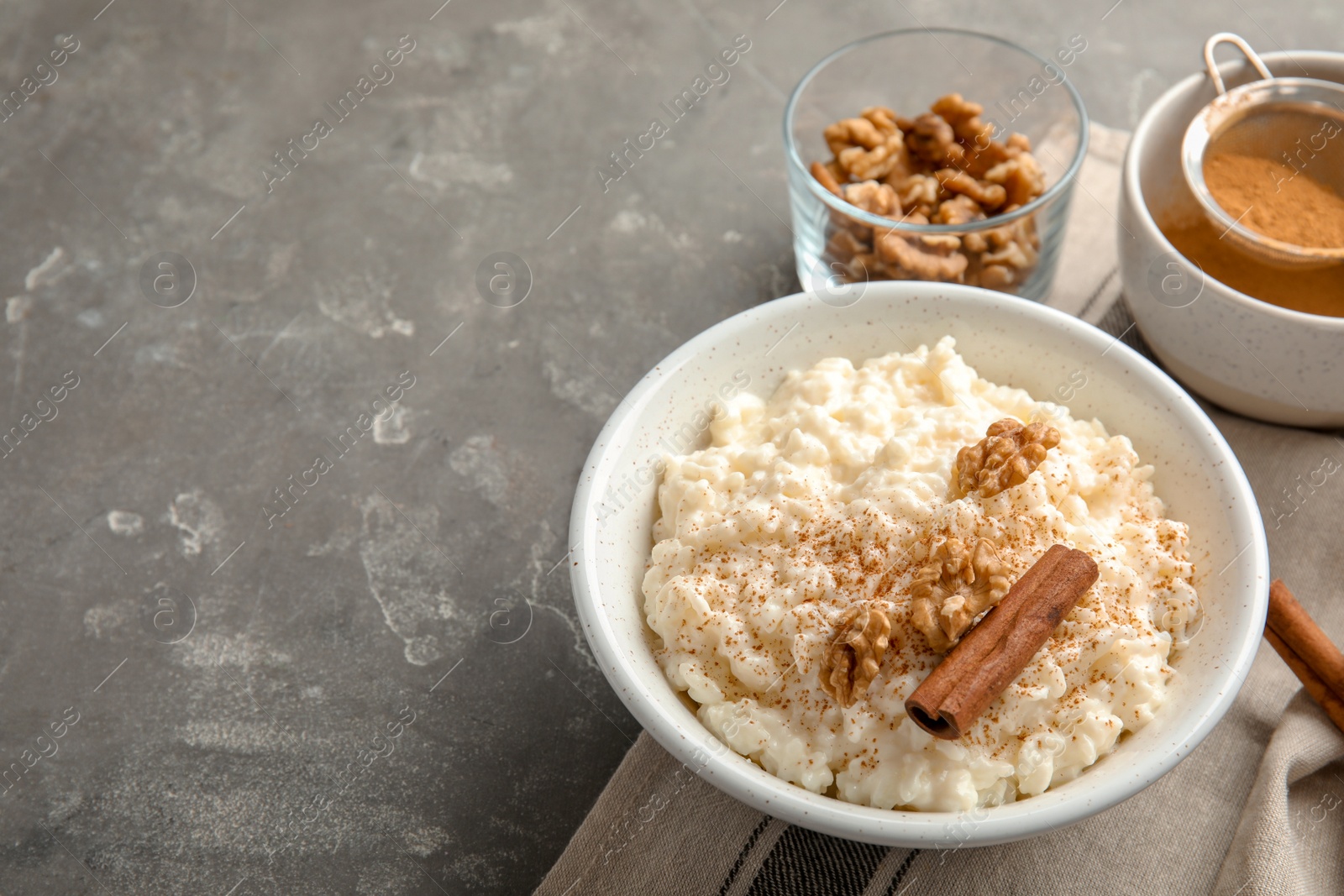 Photo of Creamy rice pudding with cinnamon and walnuts in bowl served on grey table. Space for text