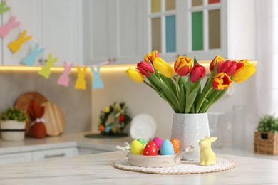 Easter decorations. Bouquet of tulips, painted eggs and bunny figure on table indoors. Space for text