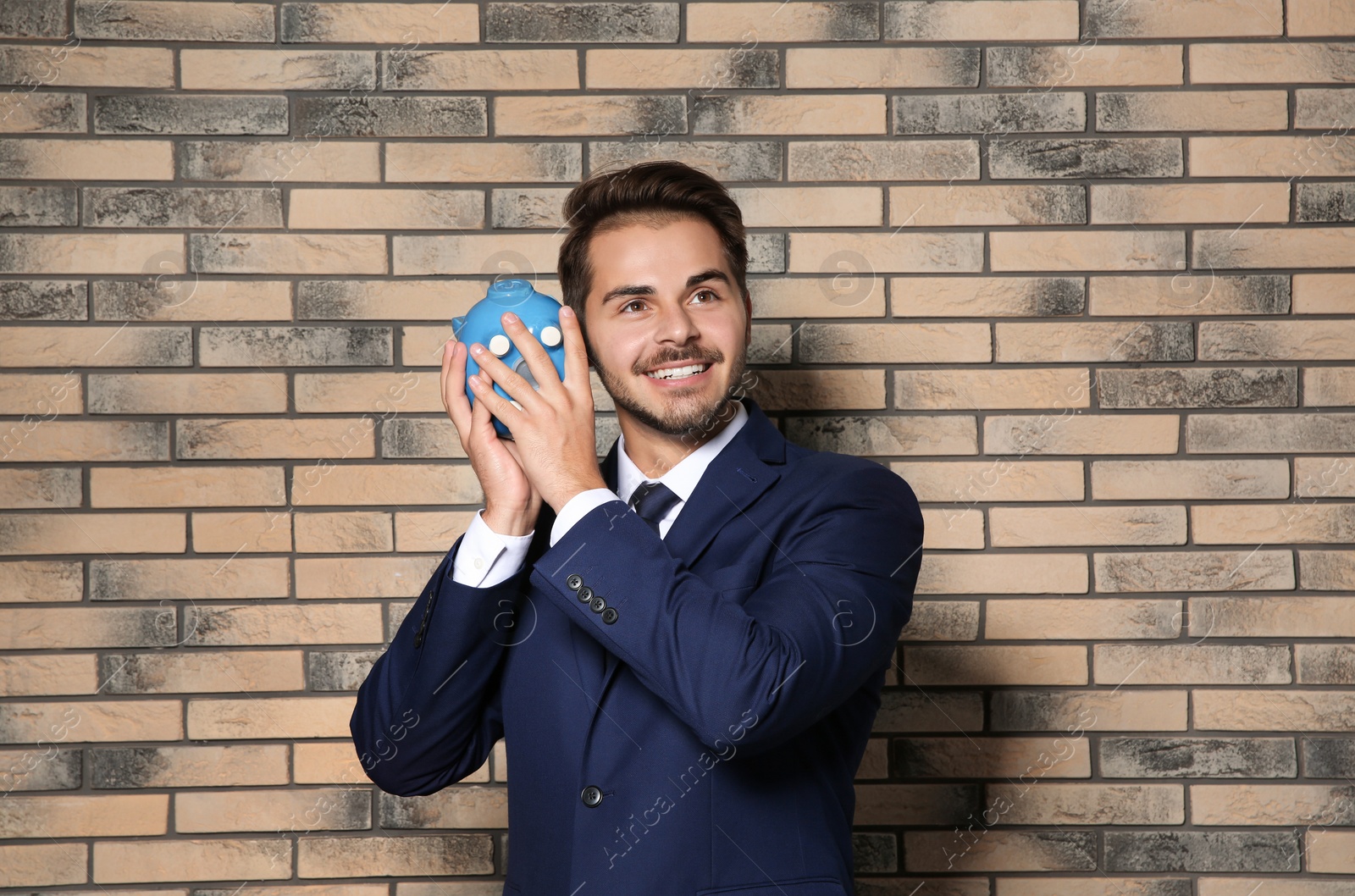 Photo of Young businessman with piggy bank near brick wall