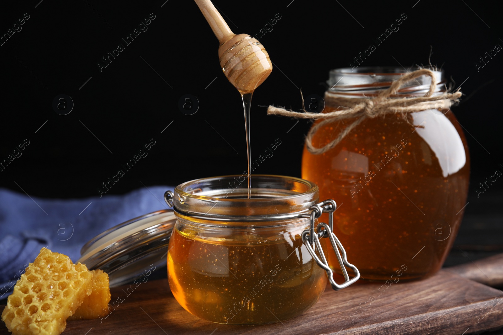 Photo of Honey dripping into jar on wooden board