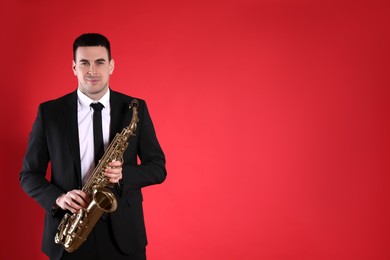 Photo of Young man in elegant suit with saxophone on red background. Space for text