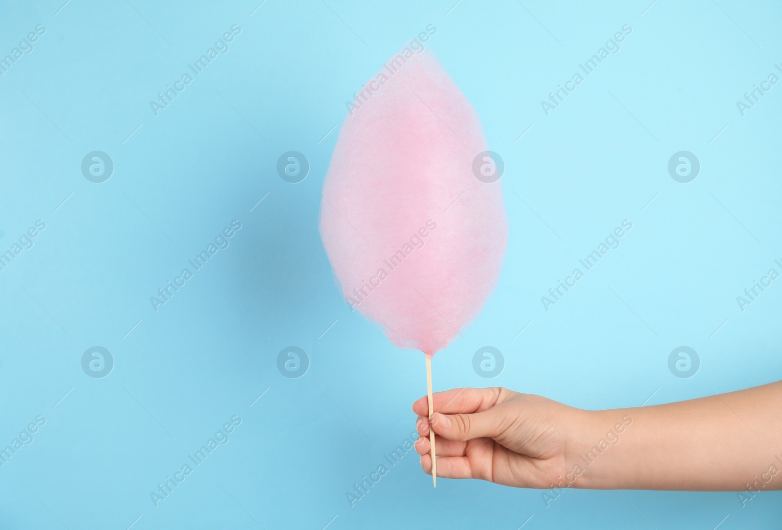 Photo of Woman holding sweet pink cotton candy on light blue background, closeup view