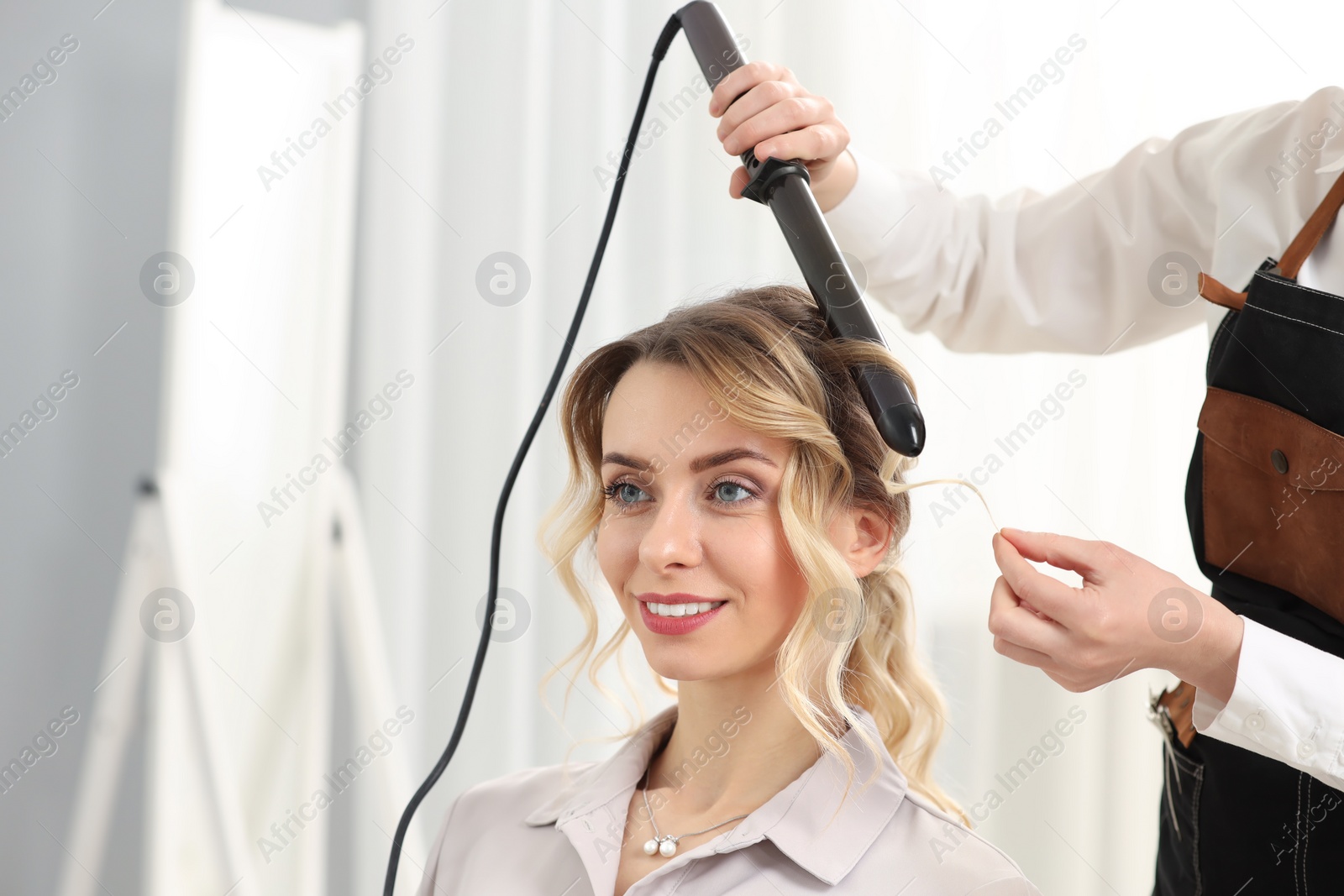 Photo of Hair styling. Hairdresser curling woman's hair indoors, closeup. Space for text