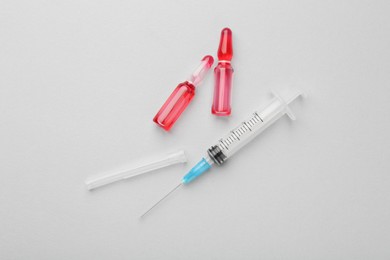 Glass ampoules with liquid and syringe on white background, flat lay