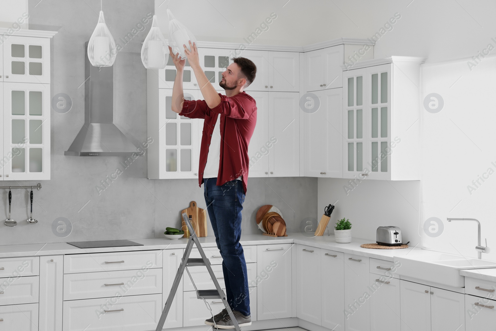 Photo of Young man installing ceiling lamp on stepladder in kitchen