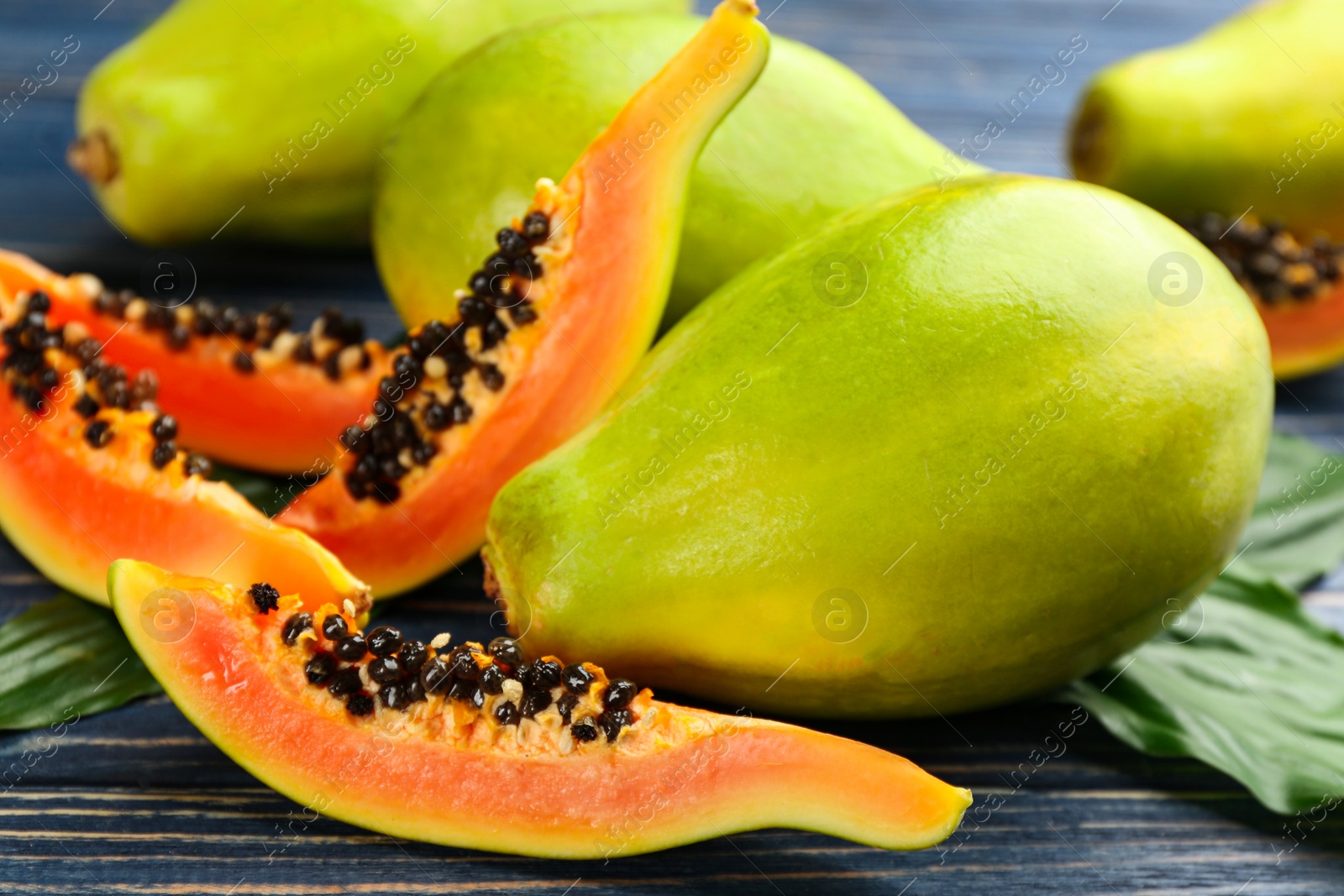 Photo of Fresh ripe papaya fruits with green leaves on wooden table, closeup