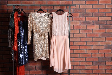 Photo of Preparing for party. Rack with collection of fashionable dresses near brick wall in showroom. Space for text
