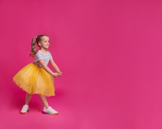 Photo of Cute little girl in tutu skirt dancing on pink background. space for text