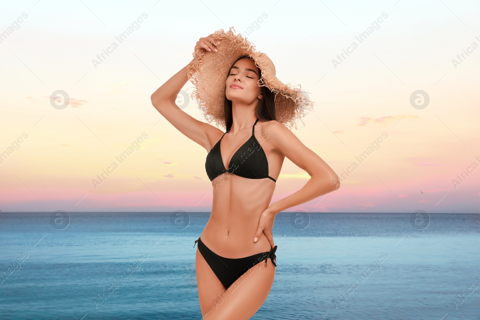 Image of Beautiful woman in stylish black bikini and hat near sea