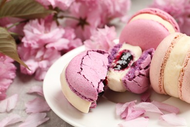 Photo of Delicious colorful macarons and pink flowers on grey table, closeup