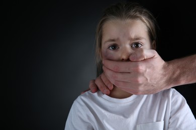 Photo of Man covering scared little girl's mouth on black background, space for text. Domestic violence