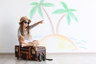 Adorable little child playing traveler with suitcase indoors