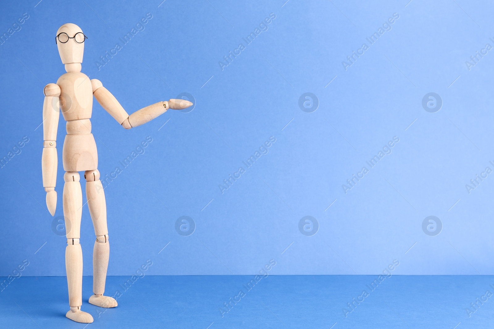 Photo of Wooden human figure in eyeglasses against light blue background, space for text