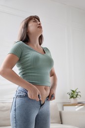 Photo of Young woman struggling to put on tight jeans at home