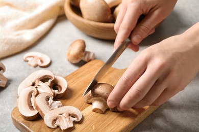 Photo of Woman cutting fresh wild mushrooms at light grey table, closeup