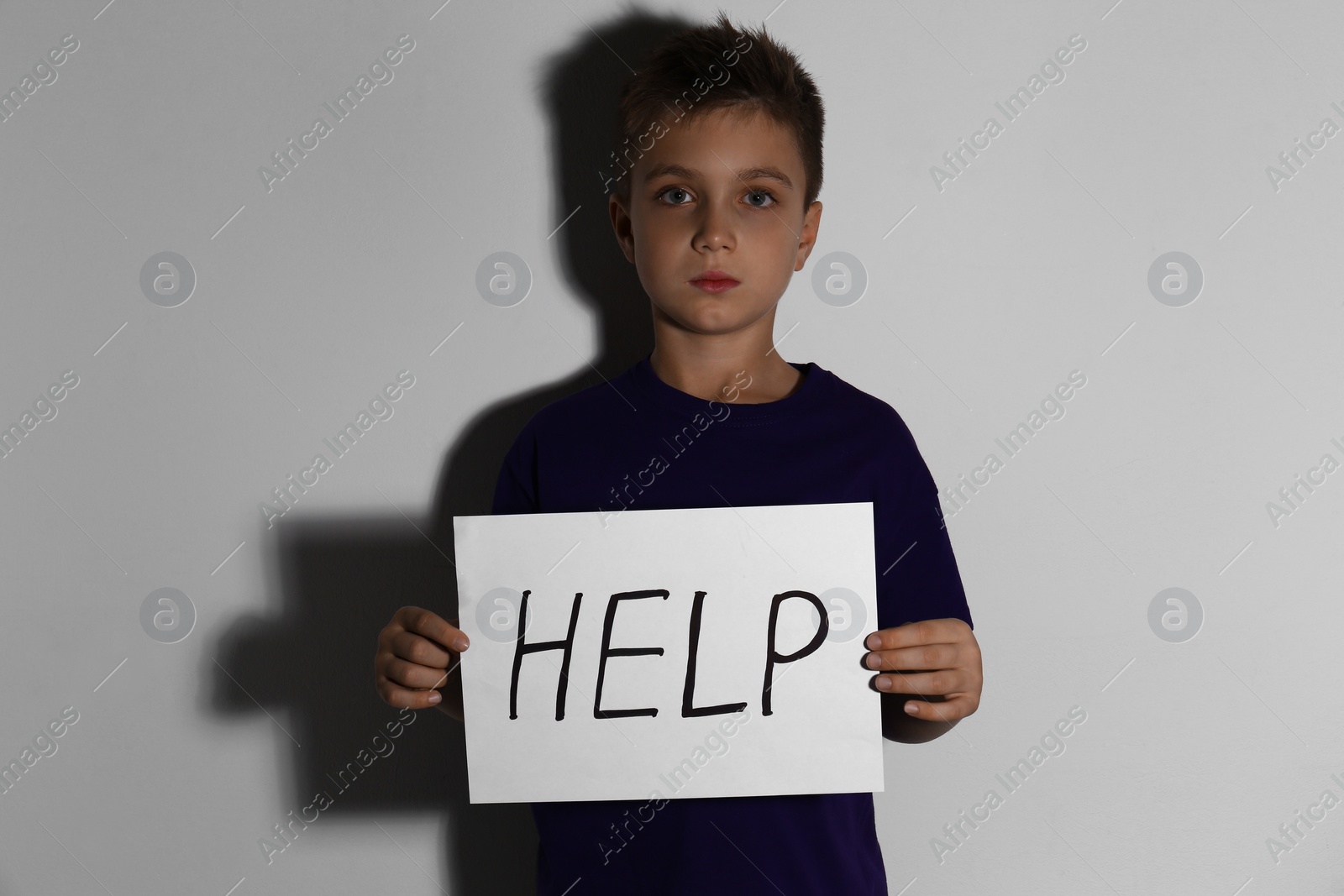 Photo of Abused little boy with sign HELP near white wall. Domestic violence concept