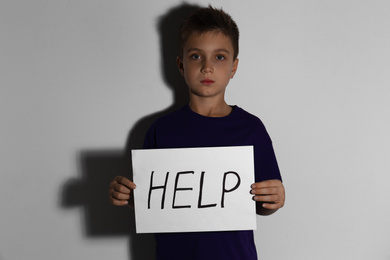 Abused little boy with sign HELP near white wall. Domestic violence concept