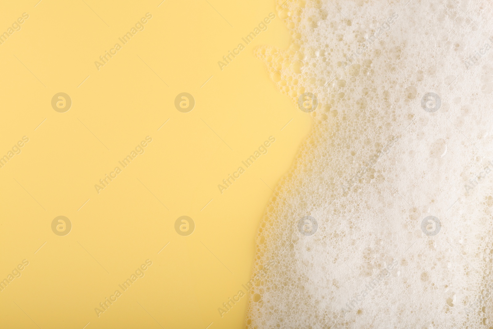 Photo of White fluffy foam on yellow background, top view. Space for text