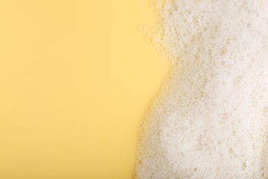 Photo of White fluffy foam on yellow background, top view. Space for text