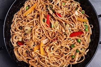 Cooked noodles with vegetables in dish on table, top view