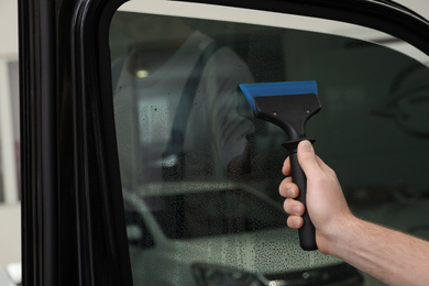 Worker washing tinted car window in workshop, closeup