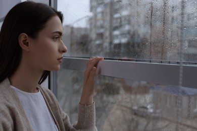 Photo of Melancholic young woman looking out of window on rainy day, space for text. Loneliness concept