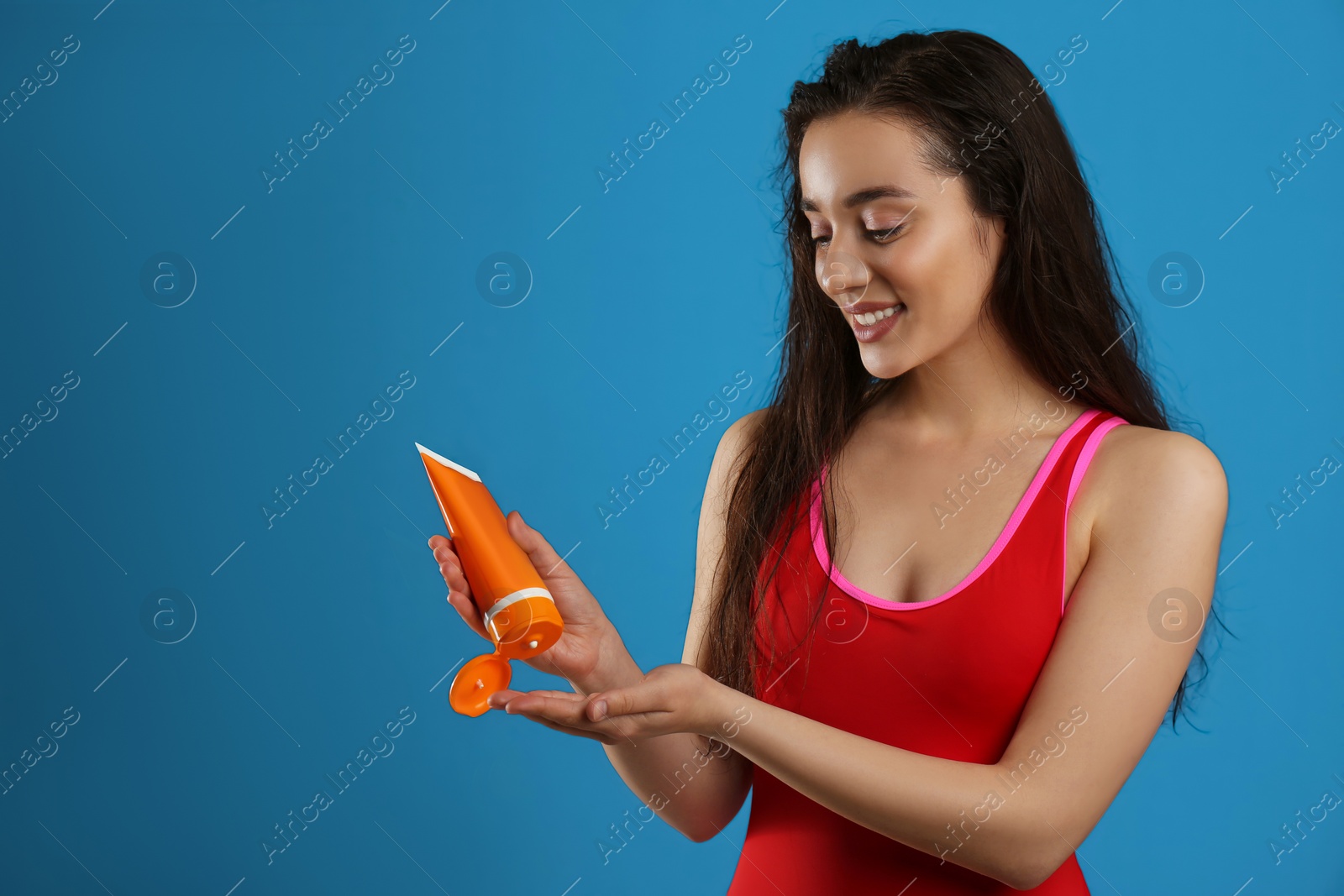 Photo of Young woman applying sun protection cream on dark blue background