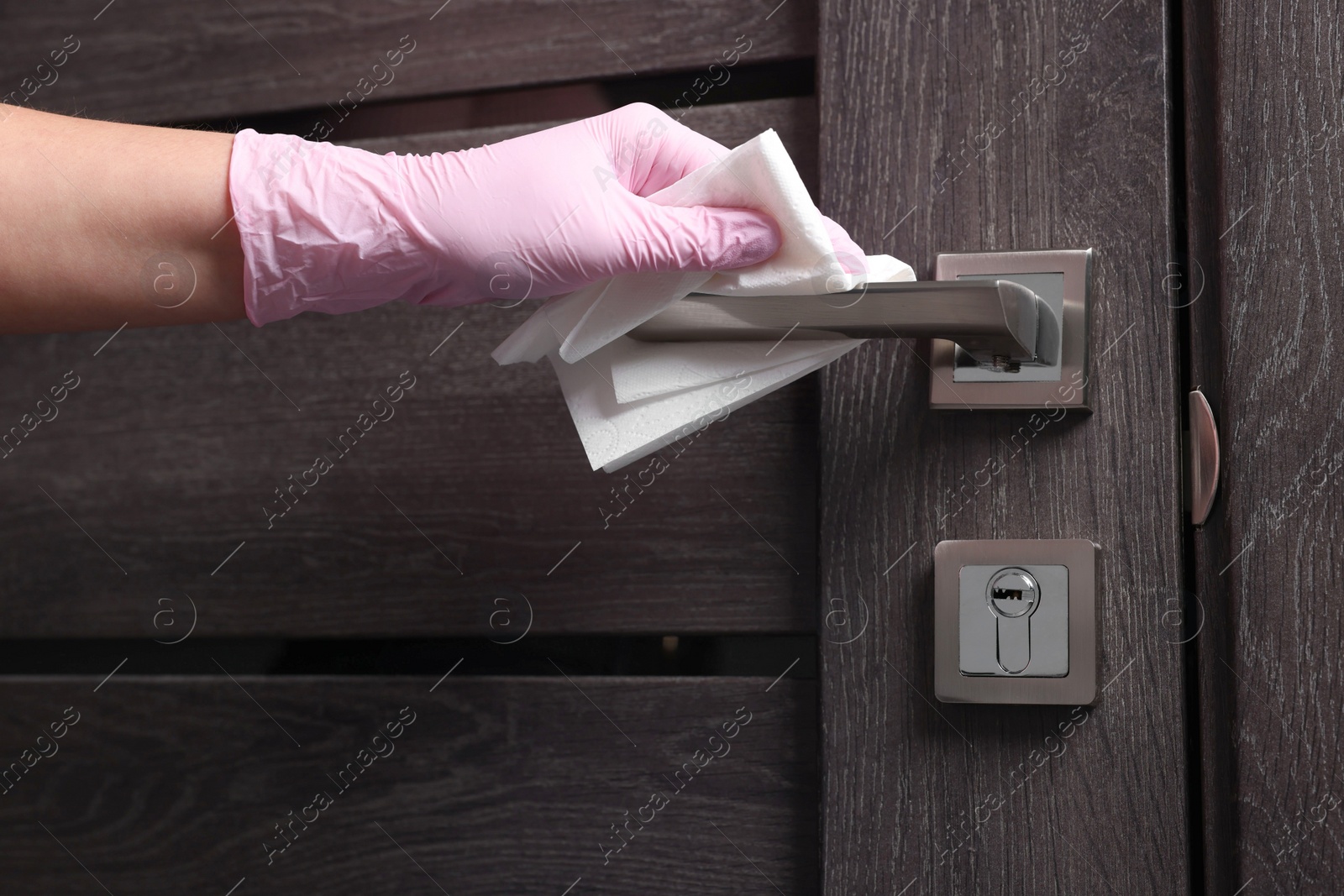 Photo of Woman wiping door handle with paper towel, closeup