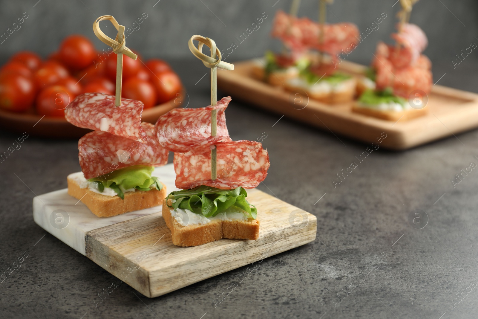 Photo of Tasty canapes with salami, greens and cream cheese on grey table. Space for text