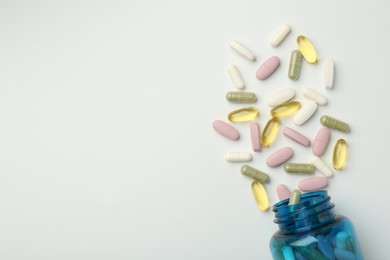 Photo of Vitamin pills and bottle on light background, top view. Space for text