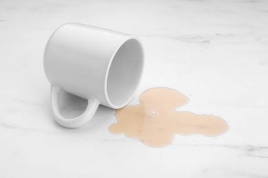 Photo of Puddle of liquid and overturned mug on white marble table