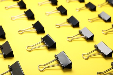 Black binder clips on yellow background. Stationery items