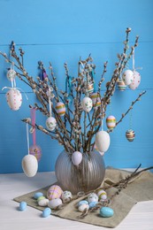Photo of Beautiful willow branches with painted eggs in vase on white wooden table. Easter decor