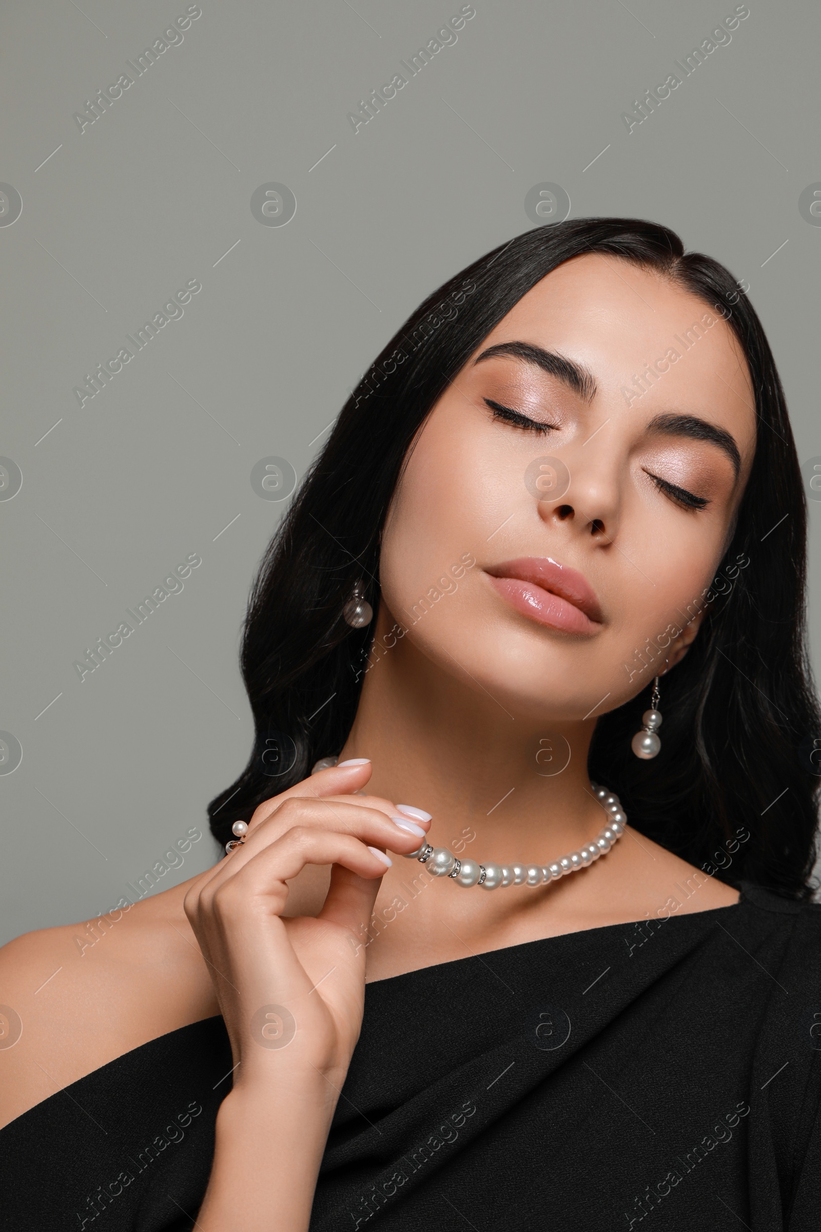 Photo of Young woman wearing elegant pearl jewelry on grey background