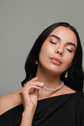 Young woman wearing elegant pearl jewelry on grey background