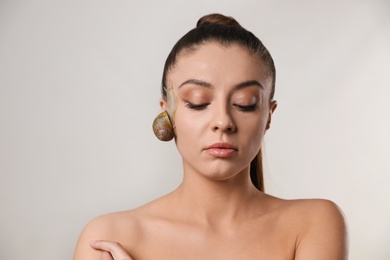 Beautiful young woman with snail on her face against grey background