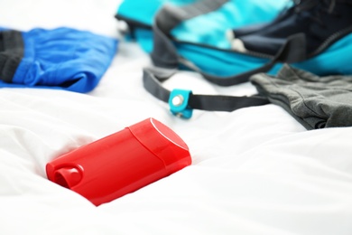 Photo of Deodorant and gym clothes on white fabric, closeup