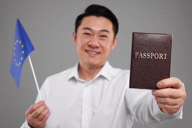 Photo of Immigration. Happy man with passport and flag of European Union on grey background, selective focus