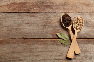 Photo of Spoons with black and white peppercorns on wooden background, top view. Space for text