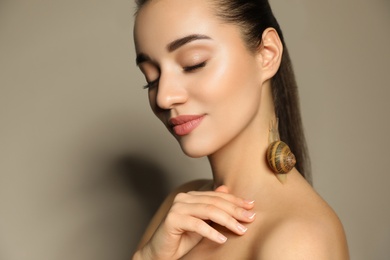 Beautiful young woman with snail on her neck against beige background