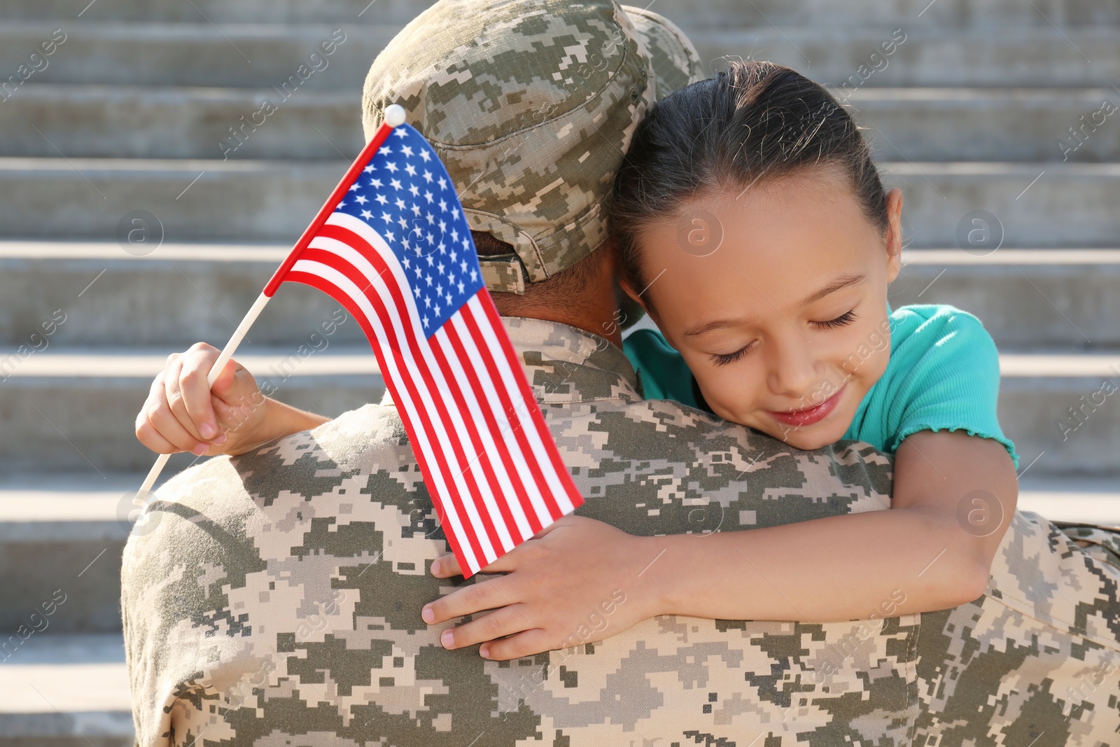 Photo of Soldier and his little daughter with flag of USA hugging outdoors