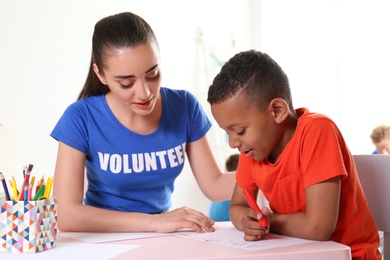Photo of Little African-American boy learning alphabet with volunteer at table indoors