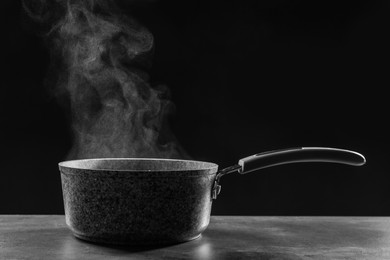 Steaming saucepan on grey table against dark background