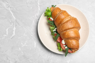 Photo of Tasty croissant sandwich with feta cheese and tomato on light grey marble table, top view. Space for text