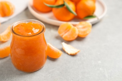 Tasty tangerine jam in glass jar on light grey table. Space for text
