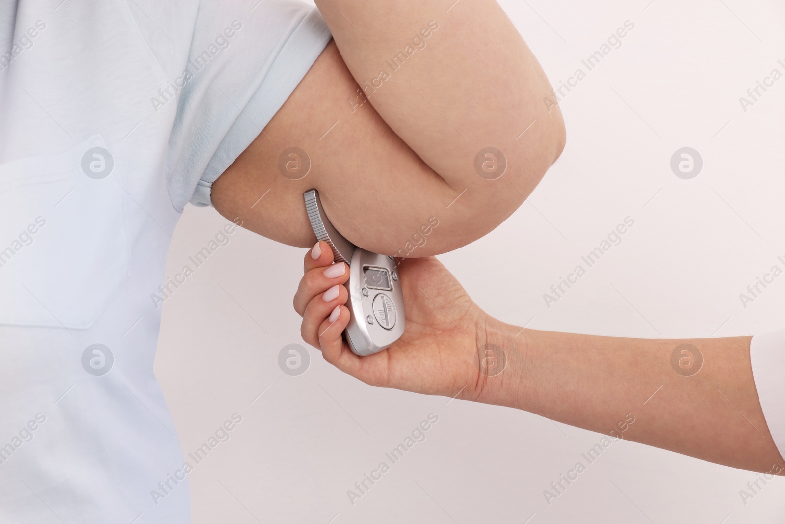 Photo of Nutritionist measuring overweight woman's body fat layer with caliper on white background, closeup